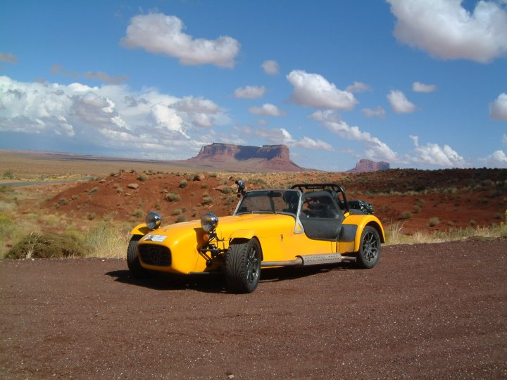 Not enough pictures on this forum - Page 3 - Caterham - PistonHeads - The image showcases a striking yellow sports car parked on a rocky terrain. The car is facing the camera, positioned on a dirt road that leads into a picturesque desert landscape. The surrounding environment is characterized by majestic sandstone rock formations and flat, rugged terrain, indicative of a dry, arid climate. The clear blue sky above adds a serene backdrop to the scene.