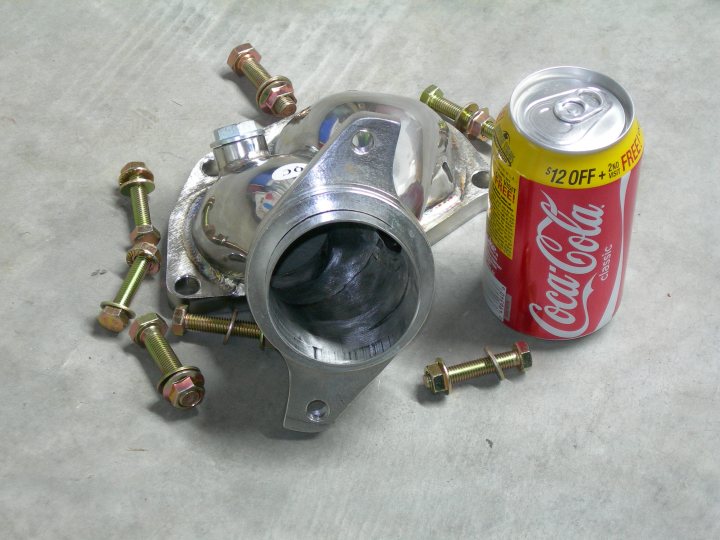 The image showcases a mechanic's scene on a concrete surface. Prominently, there is a labeled Coca Cola can, featuring the familiar red and white color scheme. To the left of the Coca Cola can, there is a collection of loose mechanical parts. Among these parts are several hexagonal fittings, small screws, and cylindrical objects. The image also contains two screws with a wing nut located on the right side. Scattered among the components are two split pins and two washers with red locks, enhancing the complexity of the scene. The overall setting suggests some sort of repair or disassembly process underway.