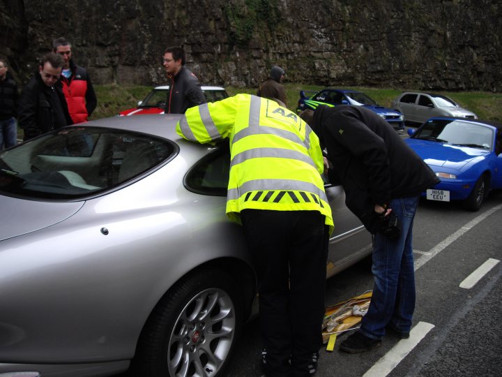 Competitionmatthehe Pistonheads - This image depicts a traffic-related incident on a road with several onlookers. The central focus is a silver car that has sustained damage, specifically to the rear, as indicated by the noticeable dent and tire marking. Two individuals, presumably emergency personnel or the accident's responders, are examining the car in front of a blue vehicle and near parked cars on the side of the road. The bystanders appear to be observing the scene, suggesting a public location and possibly a minor accident involving the silver vehicle.