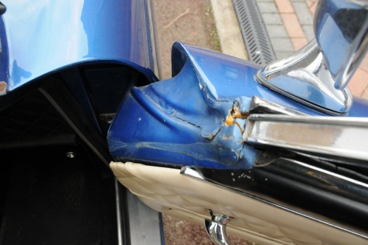 Any Gordon Keeble Owners Out There? - Page 11 - Classic Fibreglass - PistonHeads - The image shows a blue car with a dented side panel, indicating that there has been an impact. The dent is located on the side door area of the vehicle, close to the point where it opens. The car is outside, as suggested by the visible road, and there's a silver hinge visible on the door. The overall scene suggests a minor car mishap that may require repair.