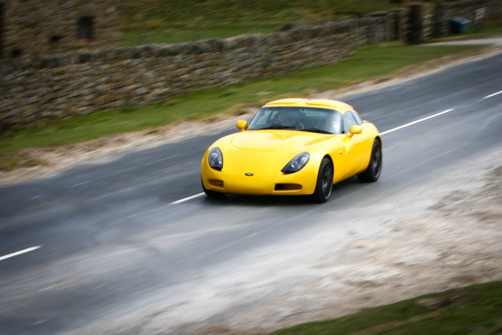 Nice Car Photo locations Middlesbrough Area? - Page 1 - North East - PistonHeads - The image showcases a vibrant yellow sports car swiftly driving down a curvy road. The road is flanked by a stone wall, adding a rustic charm to the scene. The misty atmosphere suggests that the photo could have been taken early in the morning or during a light rain. The car's driver appears focused, maintaining control as the car navigates the winding path.