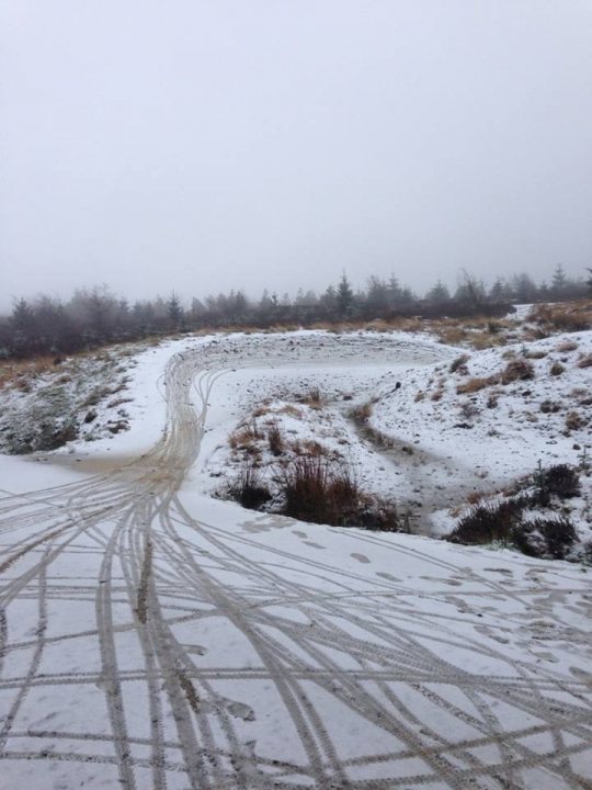 Pistonheads - The image depicts a winter scene where the ground is covered with a layer of fresh snow. There are tire tracks in the snow, suggesting that someone recently passed by, possibly on a vehicle. The tracks lead towards a hill in the distance, where there appears to be an ice patch or a small puddle of water surrounded by snow, indicating that the hill might be an ice-covered or melting area. There's a line of trees along the left side of the image, the tips of which are pointing upwards, possibly indicating a harsh weather condition or the presence of a field or a farm behind the hill. The sky is overcast and dreary, suggesting a very cold or chilly day. There's a solitary figure visible on the top right corner of the image, but it's too indistinct to make out any specific details about the person.