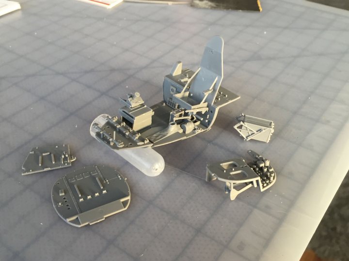 Tamiya 1/32nd Mosquito FBIV - build! - Page 1 - Scale Models - PistonHeads - The image showcases a tabletop scene where several mini models are meticulously arranged. Central to the scene is a space ship model, complete with a character seated inside its open hatch. To the left of the ship, there's a partial hull model that appears to belong to the same spacecraft. On the right, two additional models are placed; one of them resembles a gun turret, while the other seems to be another hype of corrugated metal suggested to be the floor. The models are primarily gray and white, with some parts showing a metallic sheen, suggesting that these could be 3D printed or hand-crafted model parts. Overall, the scene suggests a serious or enthusiastic modeler at work.