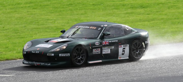 Pistonheads - The image captures a moment of intense concentration on a race track. A cheerful green sports car, the number 5 prominently displayed, is in the midst of taking a right turn. The vehicle is adorned with multiple stickers, including logos for Pirelli and Recaro, adding to its competitive appearance. The white spray left behind by the car's tires emphasizes the speed at which it's going, with the ground blurred from its swift motion. This exhilarating scene encapsulates the thrill and precision involved in car racing.