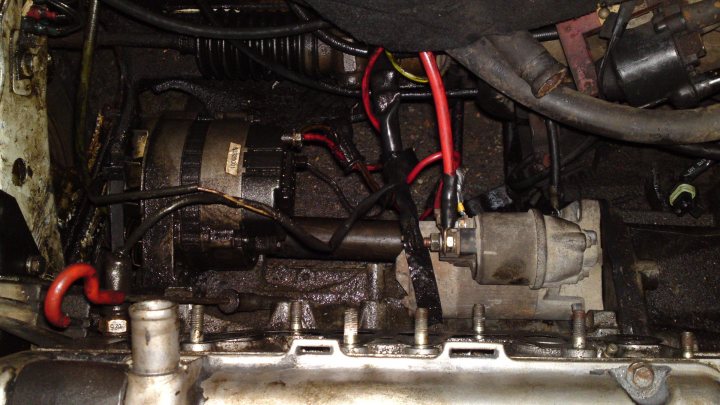 A bike parked next to a pile of luggage - Pistonheads - The image shows an engine compartment with various mechanical parts and wires. The focal point is an exposed, metallic component resembling a part of the engine's cooling system, which is suspended from the car's hood and connected to several red wires and black tubes. The engine appears to be an internal combustion engine, characterized by its metal casings and the shaped elements visible. The wires indicate that the engine might be undergoing maintenance or repair, as suggested by the visible connections. The overall state of the components suggests that it could be a close-up view of a worn or serviced engine.