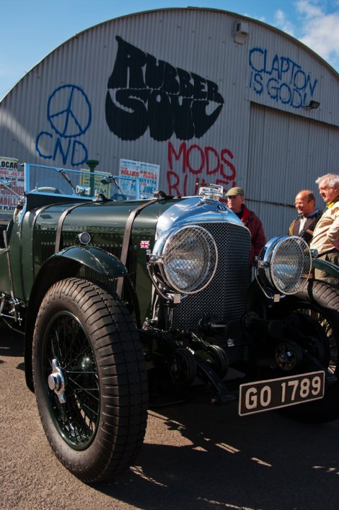 Everything But The Car - Page 1 - Goodwood Events - PistonHeads - The image showcases a vintage military truck, painted in a blend of vibrant green and white, proudly bearing European registration plates. The truck is parked under a roof advertising Roller Skating, suggesting a juxtaposition between the leisure activity and the military history associated with the vehicle. Around the truck, onlookers stand, adding a sense of scale and context to the image. The focus on the wheels of the truck in the foreground draws attention to the robust structure that can be inferred as essential for the vehicle's functionality, harking back to a time of global conflict, sturdy vehicles, and roller skating as a popular form of entertainment.