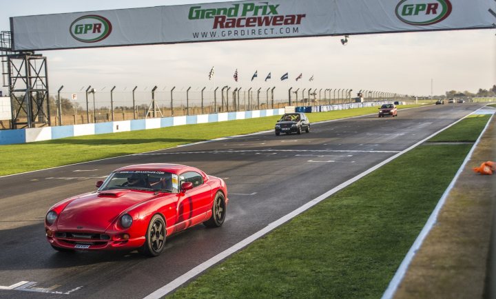 Your Best Trackday Action Photo Please - Page 85 - Track Days - PistonHeads - In the image, a red sports car is driving past a large advertisement on a race car track. The advertisement prominently displays the words "Grand Prix Racewear" and "GPR Direct.com". There's a green field visible in the background, indicating that the track is outside a city. Additionally, there are several other cars racing on the track, further emphasizing the sporting event taking place.