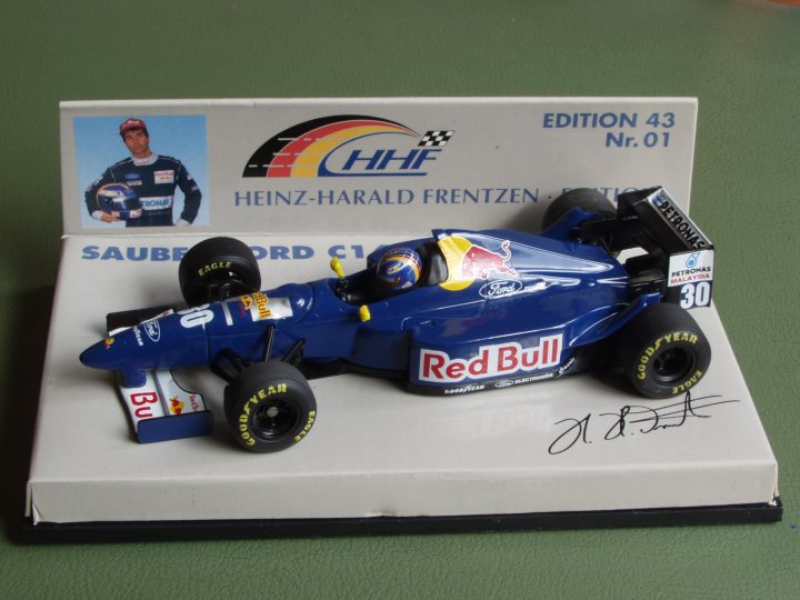 Collection Pistonheads - The image shows a small blue toy race car sitting on a white stand or box. The car features the Red Bull logo prominently on its side and has other sponsors like Heinz-Harald Frentzen, Sauber-Ford, and Goodyear visible on it. A person's signature, possibly that of a racing driver or an fan, is present on the box, alongside the logo of HHF (drinks company Heineken-Harald Frentzen). The setting appears to be a display or a collector's display case.