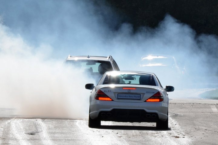 Why are there so few car photographs? - Page 8 - Photography & Video - PistonHeads - The image shows a smoke-filled city street where a white car is driving quickly. Behind the white car is another vehicle, also in motion, contributing to the smoke due to a dusting or some other event causing visible exhaust. There is another vehicle visible at the front of the image, but it appears to be at a distance or out of focus. The scene seems to capture an active, urban environment with a focus on vehicular motion and emissions.