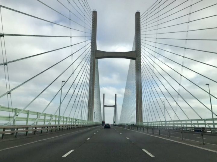 The Wales 450 - A short blog *Pics Added* - Page 1 - Roads - PistonHeads - The image captures a spectacular view of the Washback Bridge, a prominent structure in the city of Belfast, Northern Ireland. The bridge is an impressive four-span cable-stayed design, known for its distinctive "X" shape tower. The photo is taken from the perspective of someone driving on the bridge, facing towards the bridge's center. In the foreground, the black banister separates the lanes, while a blue and white sky filled with clouds forms a stunning backdrop. The image conveys a sense of freedom and the marvel of human engineering.