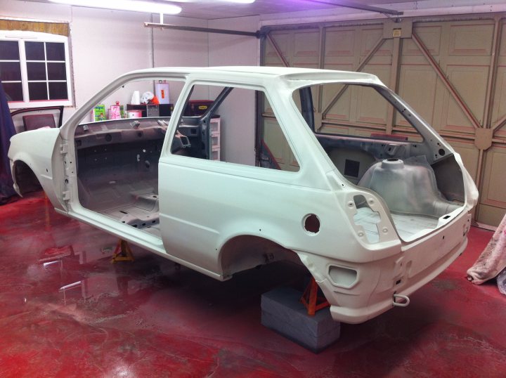 Pistonheads - The image illustrates a large work area where a white car is the centerpiece. The car itself seems to be in mid-assembly, given its disassembled state and the presence of several disconnected parts around it. The floor is red, and the walls and ceiling are also visible, indicating a well-lit and spacious workshop environment. The variety of tools and equipment scattered around suggests that this is a professional setting designed for vehicle customization or repair. The absence of moderate to severe damage is noticeable while seeing this image. Overall, the scene conveys the process of car servicing or modification in a professional setting.