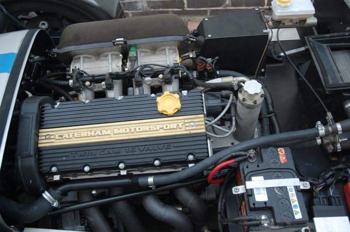 Pistonheads Caterham - The image captures an engine compartment filled with body components. A large inverter connector, painted in two shades of yellow, is prominently visible in the center. This inverter is a prominent feature in the otherwise mechanical setting. On either side of the inverter, there are large, dark hoses and a black component with various silver and red accents. The engine bay appears to be open, providing a clear view of the components within.